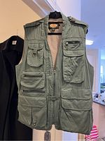 Front view of the green Woolrich men's sports vest showing multiple pockets with zippers and flaps, shoulder epaulets, and front zip and snap closures.