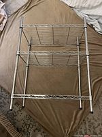 Metal wire shelving unit with three tiers shown from the front, photographed on a brown fabric surface.