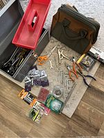 Overview of the metal tool chest with tools inside, fabric tool bag, hand tools on mat, and miscellaneous hardware items on floor.