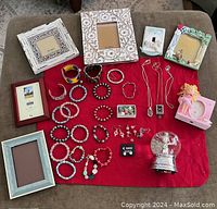 Full lot overview including jewelry, snow globe, picture frames on red cloth background.