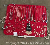 Overview of assorted jewelry laid out on red cloth including necklaces, rings, bracelets, earrings, and a watch.