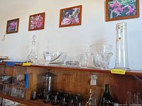 Crystal decanter, bowls, bell and china plates on a wooden cabinet with floral paintings above