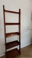 Front view of wooden ladder shelf with wool scarf placed on middle shelf against white wall
