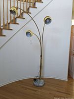 Front view of the three-light brass tone floor lamp with marble-look base, placed near a staircase with wooden handrails.