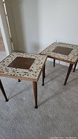 Pair of square mid-century modern side tables with wood grain centers and mosaic tile borders, front view.