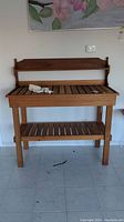 Front view of potting table showing overall structure, slatted top and lower shelf with decorative items placed on surface