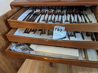 Two wooden drawers filled with assorted silverplated flatware including forks, spoons, knives, and specialty pieces arranged neatly on white liners.