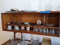 Shelf with porcelain teacups, saucers, trinket dishes, glassware beneath a wooden cabinet