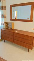 Full front view of six-drawer teak dresser with mirror mounted above.