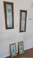 Two larger floral prints hang on the wall with ornate gold frames and glass.