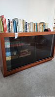 Front view of the wooden cabinet with frosted sliding glass doors showing some reflection and books on top.