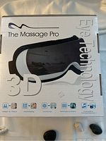 Box of The Massage Pro 3D Eye Massager showing printed product features such as intelligent air pressure, infrared heating, point massage, multi-frequency vibration, and soothing music.