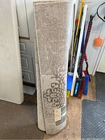 Rolled beige and taupe patterned rug leaning vertically with label visible.