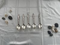 Five silverplate spoons laid out side by side showing full spoons and figurines on handle tops