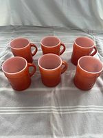 Top and angled view of six rust orange barrel ranger style mugs with handles, showing the smooth surface and color consistency.