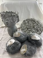 Photo showing four bags of river rocks, the ladies head flower pot and decorative garden stone plaque together.