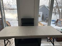 Full view of the folding table in open position showing the tabletop and a chair behind it.