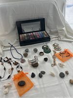 Full lot overview including jewelry pieces arranged on a white cloth with an eyeshadow palette in the background, includes rings, necklaces, bracelets and earrings.
