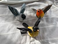Three colorful magnetic bird figurines shown on cloth background, wings spread as if flying, tagged with Koppers brand label.