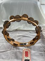 Full front view of the tambourine showing the natural wooden frame, double row of jingles, and attached sale tag.