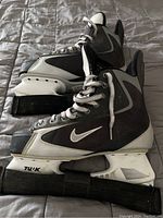 Side view of black and grey Nike ice hockey skates with white boyle blade holders and black skate guards attached.