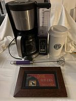 Ninja coffee maker with water reservoir and digital panel, Starbucks ceramic coffee container with lid, milk frother with purple handle, framed Old Crow coffee sign