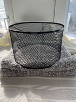 Photo of a black metal mesh lampshade with round shape and diamond-pattern design on top of a gray bathmat.