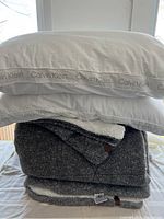 Stack of 2 brand new Calvin Klein king pillows with white pillowcases featuring Calvin Klein brand repeated along edges. Bottom contains folded reversible Sherpa comforter in grey and white.