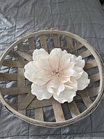 Round wooden tobacco basket with large white flower decor in the center, showing petal details and basket slats.