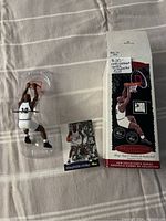 Photo of the ornament in plastic packaging, the collector card beside it, and the box standing upright nearby.