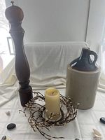 Photo showing large ceramic jug, tall wooden peppermill, pillar candle and decorative willow wreath on white cloth background