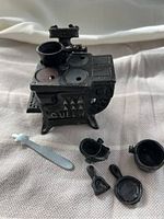Photo showing cast iron miniature Queen stove with detailed top burners and included pots, pan, shovel, coal bucket, and flat tool.