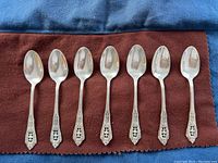Full set of seven Wallace sterling silver teaspoons laid out evenly on cloth.