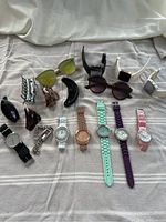All watches, sunglasses, and hair clips displayed on beige surface, clearly showing colors and styles of all items in the lot.
