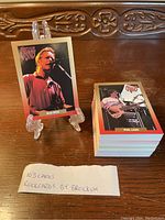 Photo showing a single card featuring Bob Weir on a clear stand next to a large stack of remaining cards