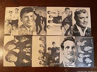 Set of 12 black and white 1960s Billboard promotional cards laid out on a wood surface showing multiple artists and groups