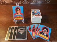 Photo of various 1978 Superman cards and stickers spread on a table with cards showing portraits of Superman and Clark Kent and Superman logos.