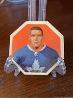 Front view of the Tim Horton hockey card showing portrait in Toronto Maple Leafs uniform with an orange background.