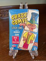 Front side of a sealed 1967 Crazy Comic Stick-Ons wax pack featuring colorful comic-style artwork and branding by Swell.
