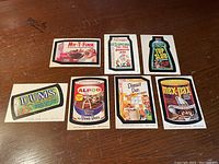 Photo showing seven 1974 Wacky Pack 7th Series parody product label cards arranged on a flat surface.