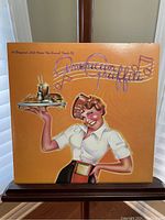 Front cover of American Graffiti soundtrack showing waitress illustration with tray and milkshake on orange background.