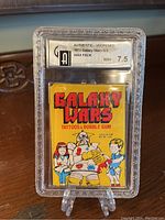 Photo showing the unopened 1973 Galaxy Wars wax pack encased in a clear grading slab with a GAI 7.5 label.