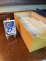Yellow box containing a large quantity of 1990's baseball and hockey sports cards neatly organized with one hockey card displayed on a stand.