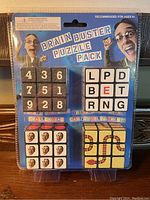 Front of sealed Brain Buster Puzzle Pack showing four small puzzle cubes with various number, letter, face, and pipe designs.