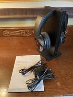 Photo of Sony wireless stereo headphone system with charging stand, power adapter, audio cable, and user manual on wooden surface.