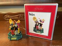 Photo of the ornament in front of its original box showing The Beatles musical figures on a green platform.