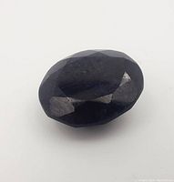 Close-up of dark blue, faceted oval sapphire gemstone showing surface details and wear.