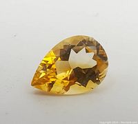 Close-up side and top view of pear shaped yellow topaz gemstone showing facets and clarity.