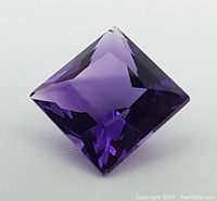 Close-up image showing the top and part of the pavilion of the square princess cut amethyst gemstone displaying its facets and deep purple color.