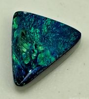 Front view of the triangular black opal gemstone showing blue and green iridescent colors